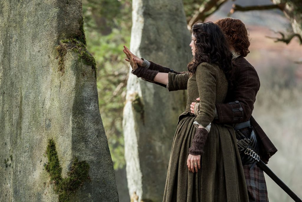 Caitriona Balfe como Claire Randall y Sam Heughan como Jamie Fraser a punto de cruzar el círculo de piedras de Craigh Na Dun en la serie Outlander. Foto de la temporada 1